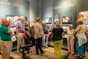 A crowd of people gathered in a small gallery listening to the photographer J. M. Giordano.