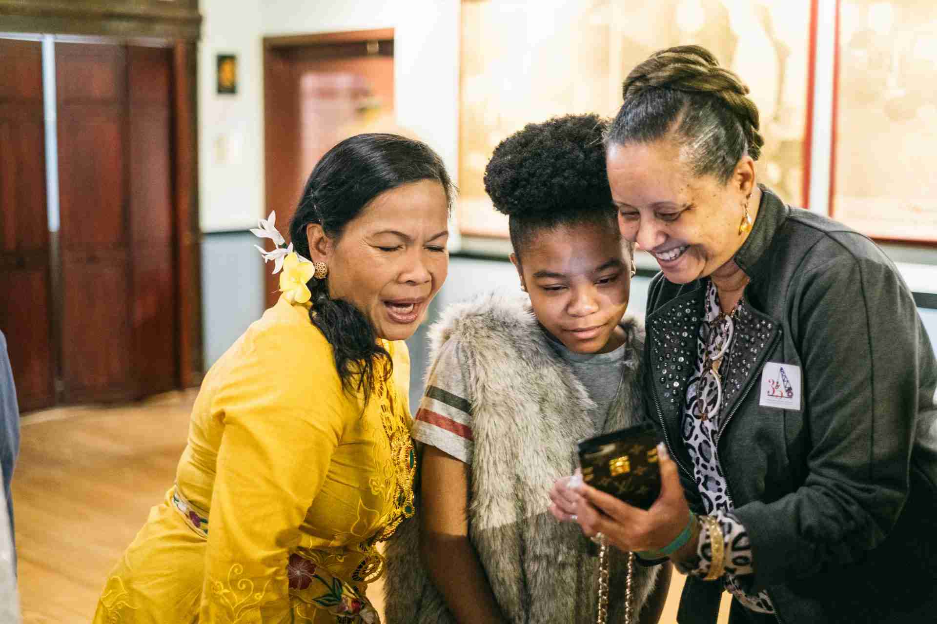 Three women look at a mobile phone and make a financial pledge to support the BMI. 